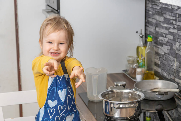 Cute uśmiechnięty chłopiec pokazuje pierścienie przed aparatem w kuchni. Poziomo. - Zdjęcie, obraz