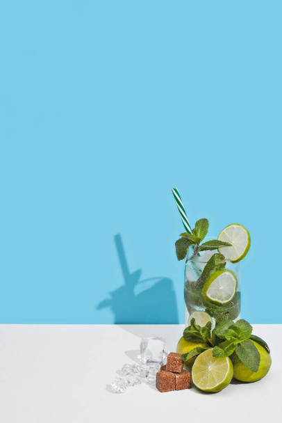 Cóctel Mojito con lima, hojas de menta y trozos de azúcar sobre doble fondo azul blanco con sombra. - Foto, Imagen