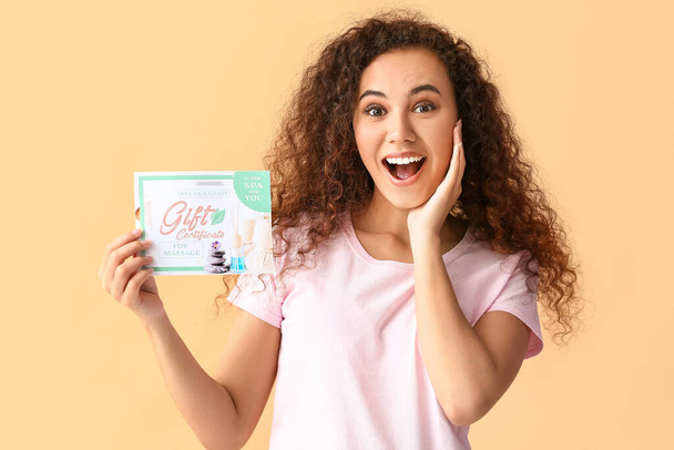 Удивлённая девушка с подарочным сертификатом на массаж на цветном фоне - Фото, изображение