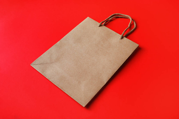 Brown paper bag with handles on red paper background. - Фото, изображение