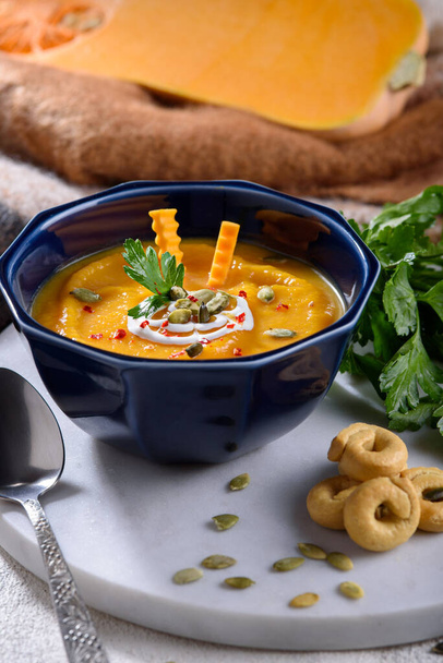 vertical pumpkin and carrot soup, cream puree soup with parsley and Italian drying taralli on white marble board, autumn seasonal dish - Photo, Image