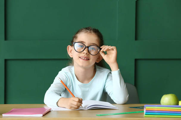 Mała dziewczynka robi pracę domową przy stole na tle koloru - Zdjęcie, obraz