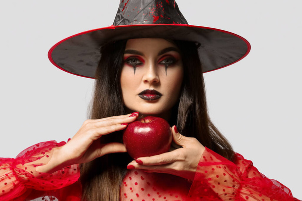 Young witch with apple on light background - Photo, Image