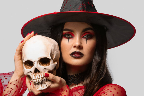 Young witch with skull on light background - Photo, Image
