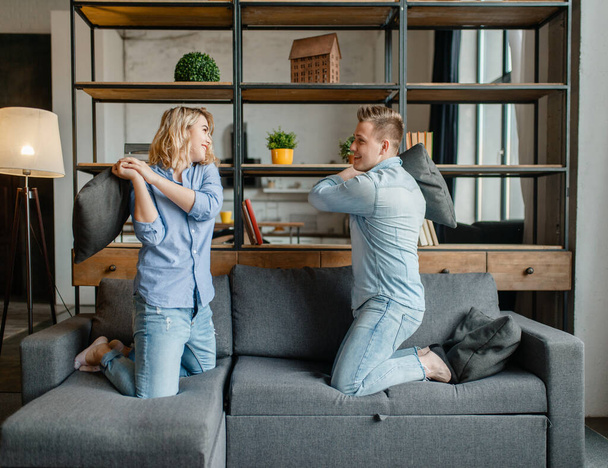 Funny love couple staged fights on the pillows. Husband and wife having fun in living room. Happy playful family resting together - Photo, Image
