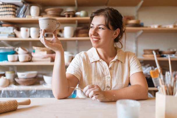 Female master holds fresh painted pot, pottery workshop. Woman molding a bowl. Handmade ceramic art, tableware from clay - Фото, зображення