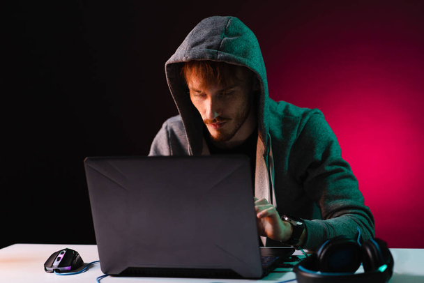 Profi-Hacker mit Laptop am Tisch auf dunklem Hintergrund - Foto, Bild