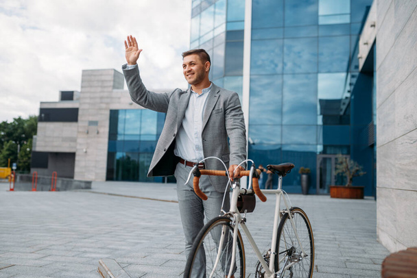 Byznysmen cyklista v obleku v centru, skleněná budova na pozadí. Obchodní osoba jízda na ekologické dopravy na ulici - Fotografie, Obrázek