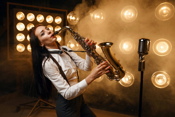 Female saxophonist plays the saxophone on the stage with spotlights. Jazz performer playing on the scene - Foto, Bild