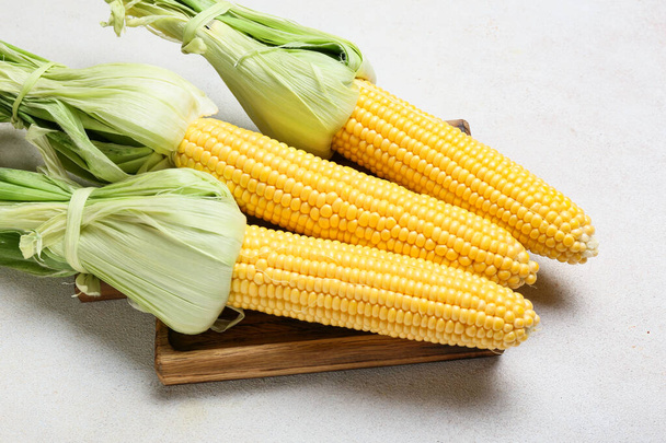 Tablero de madera con mazorcas de maíz frescas sobre fondo claro - Foto, imagen