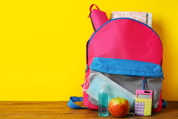 Рюкзак с яблоком и медицинская маска на столе возле цветной стены - Фото, изображение