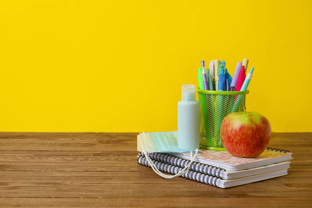 Stationery with apple and medical masks on table near color wall - Photo, Image