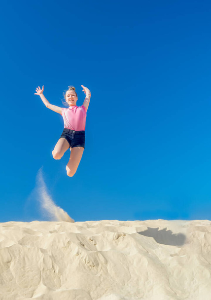 a young girl jumps in the summer from a yellow sand dune - Fotó, kép