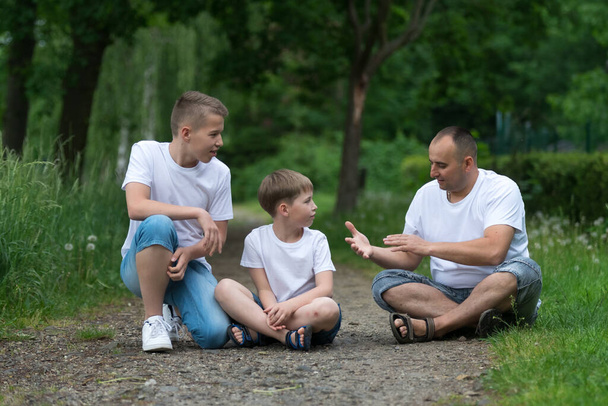 A father with his sons sits on the ground. Family portrait. - Photo, image