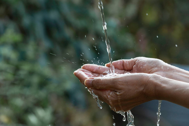 Water pouring on hand with blurred nature background. - Foto, Imagem