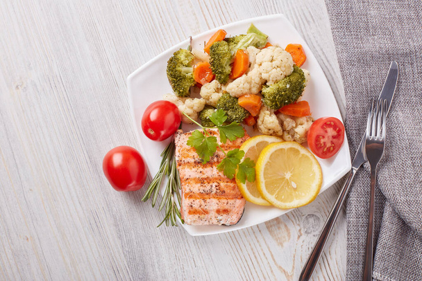 Grilled salmon fillet  garnished with vegetables, lemon, tomato, herbs lying on plate on wooden background. Top view with copy space.Healthy food. Keto diet. - Foto, Bild