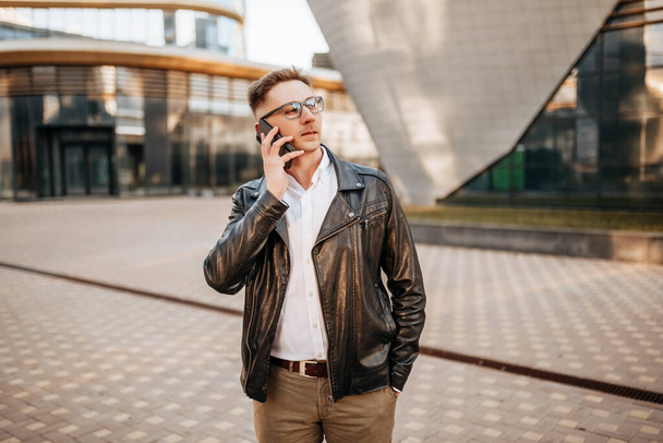 Handsome man with glasses with a smartphone on the street of a big city. Businessman talking on the phone on urban background - Фото, зображення