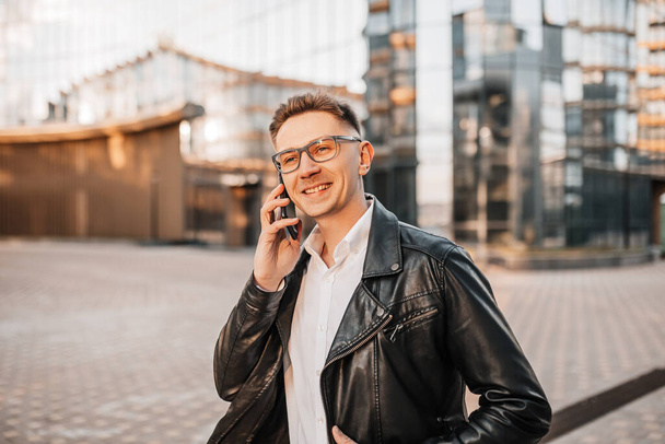 Handsome man with glasses with a smartphone on the street of a big city. Businessman talking on the phone on urban background - Фото, зображення