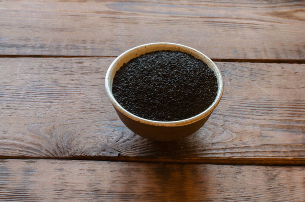 ινδικό μαύρο κύμινο σπόρους σε πήλινο κύπελλο σε ξύλινο φόντο - Φωτογραφία, εικόνα