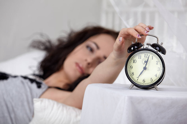 Young sleeping woman and alarm clock in bedroom at home.  Selective focus on a alarm clock. - 写真・画像