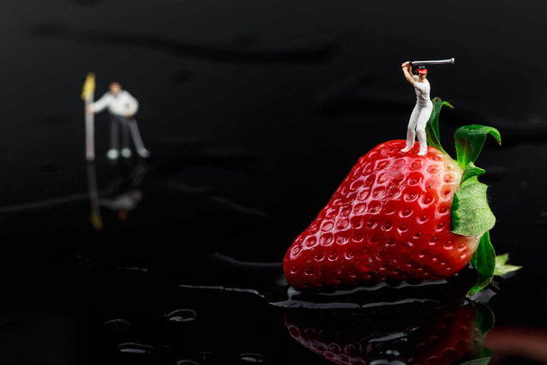 Juicy red strawberry on black acrylic glass and miniature golfer on top - Φωτογραφία, εικόνα