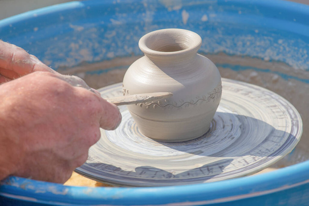 Potter's hands put a pattern on a jug on a potter's wheel - Foto, afbeelding