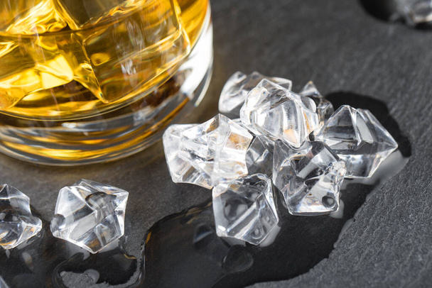 Detail of glass of whiskey and melted ice cubes on a black background - Foto, Imagem