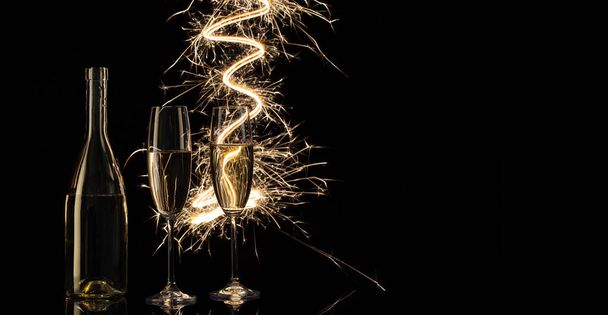 Glasses and a bottle of champagne in the shining Bengal lights. Black background. Concept of celebration and New Year. - Valokuva, kuva
