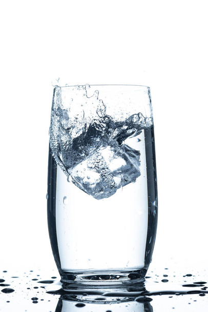 Cubo de hielo cayendo en un vaso de agua gotas de agua salpicada - Foto, Imagen