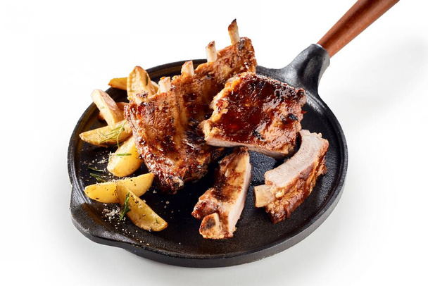 Gourmet ribs and potato wedges in a skillet pan on a white background with copy space. - Фото, изображение