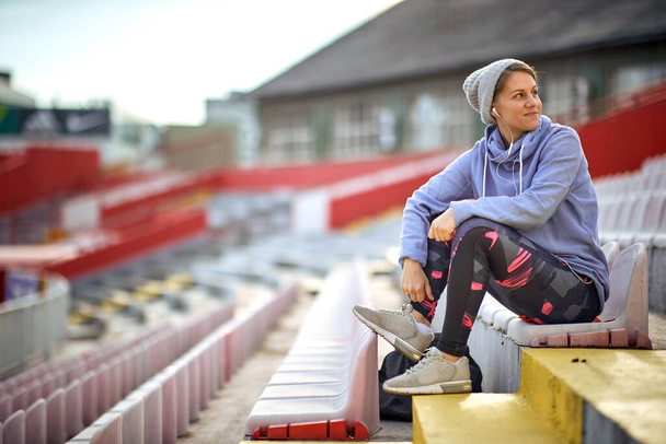 Sports woman seat on the tribune before training and listening music . Sports concept. - Foto, Bild