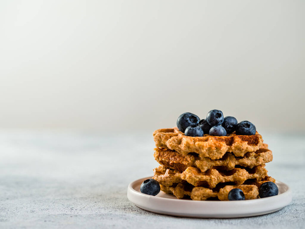 Easy healthy gluten free oat waffles with copy space. Stack of appetizing homemade waffles with oat flour decorated blueberries, on plate over light gray cement background - Foto, imagen