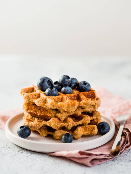 Easy healthy gluten free oat waffles with copy space. Stack of appetizing homemade waffles with oat flour decorated blueberries, on plate over light gray cement background. Vertical - Foto, Imagen