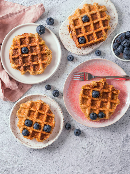 Easy healthy gluten free oat waffles with copy space. Plates with appetizing homemade waffles with oat flour decorated blueberries, on light gray cement background. Vertical. Top down view or flat lay - Фото, зображення