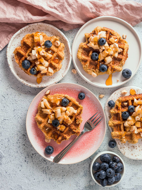 Easy healthy gluten free oat waffles with copy space. Plates with appetizing homemade waffles with oat flour decorated blueberries, bananas and honey on gray background. Vertical. Top view or flat lay - Foto, Bild
