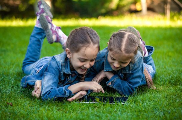 petites sœurs allongées sur de l'herbe verte et jouant sur tablette
 - Photo, image