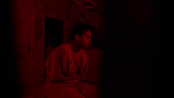 Hombre loco en camisa de fuerza volviéndose loco sentado en la cama en la celda de un hospital mental y mirando a la cámara - Metraje, vídeo