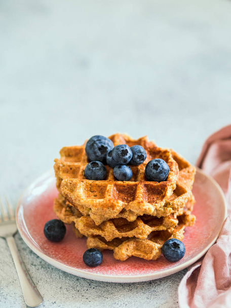 Easy healthy gluten free oat waffles with copy space. Stack of appetizing homemade waffles with oat flour decorated blueberries, on plate over light gray cement background. Vertical - Foto, Bild