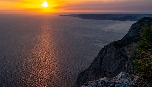 The sun setting into the sea and the long cape crashing into the Black Sea at sunset. Coast of the Crimean Peninsula near Balaklava. - Фото, зображення