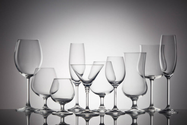 Set of glasses for different alcoholic drinks and cocktails on dark gray background. Empty clear glassware. - Photo, image