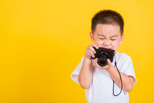 Asian Thai happy portrait cute little cheerful child boy hold photo camera compact doing taking the picture, studio shot isolated on yellow background with copy space - Zdjęcie, obraz