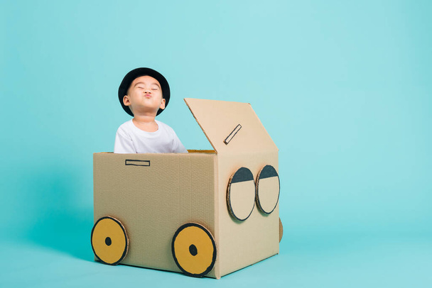 Happy Asian children boy smile in driving play car creative by a cardboard box imagination, summer holiday travel concept, studio shot on blue background with copy space for text - Foto, afbeelding