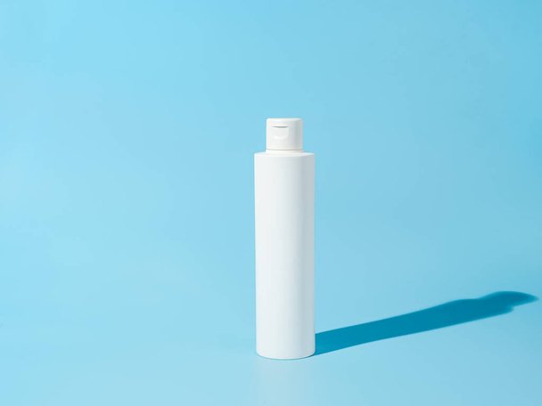 Empty white plastic bottle mockup in hard light. Blank opaque bottle without packaging on blue background. Mock up for package design - Фото, изображение