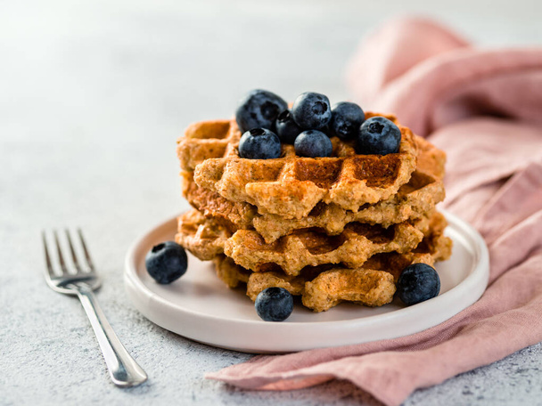 Easy healthy gluten free oat waffles with copy space. Stack of appetizing homemade waffles with oat flour decorated blueberries, on plate over light gray cement background - Foto, Imagem