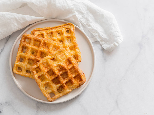Perfect savory keto waffles. Two ingredients chaffles on plate over white marble background. Eggs and parmesan cheese low carb waffles. Top view or flat lay. Copy space for text or design. - Фото, зображення