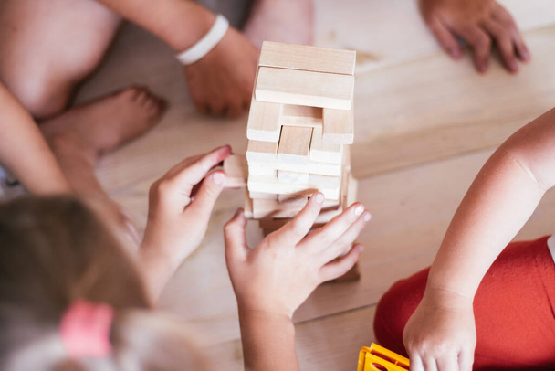 Childrens hands play game with tower made of wooden blocks - 写真・画像