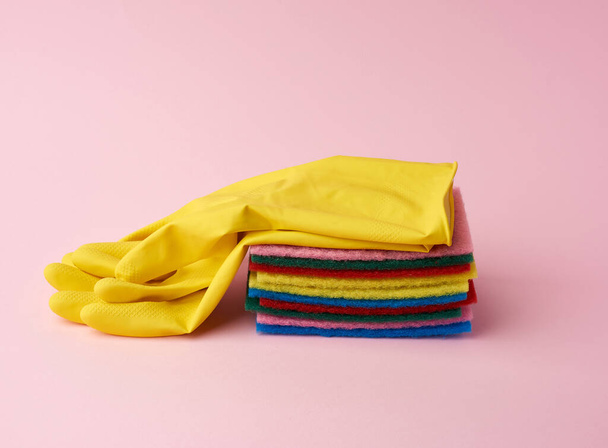 multi-colored kitchen sponge, rubber yellow gloves on a pink background, set of items for cleaning - Fotó, kép