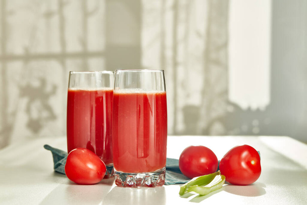 Two glasses with fresh tomato juice, celery and ripe tomatoes on white table near window. With copy space - Fotó, kép