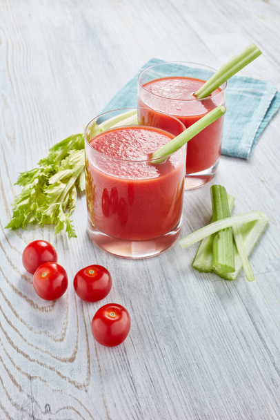 Two glasses with fresh tomato juice, celery, parsley and ripe tomatoes on light wooden background. Top view - 写真・画像