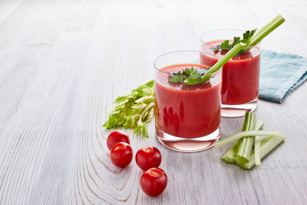 Two glasses with fresh tomato juice, celery, parsley and ripe tomatoes on light wooden background. Top view - Φωτογραφία, εικόνα